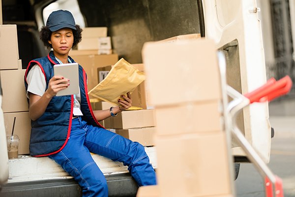 black-female-deliverer-going-through-check-list-touchpad-while-checking-delivery-package-truck